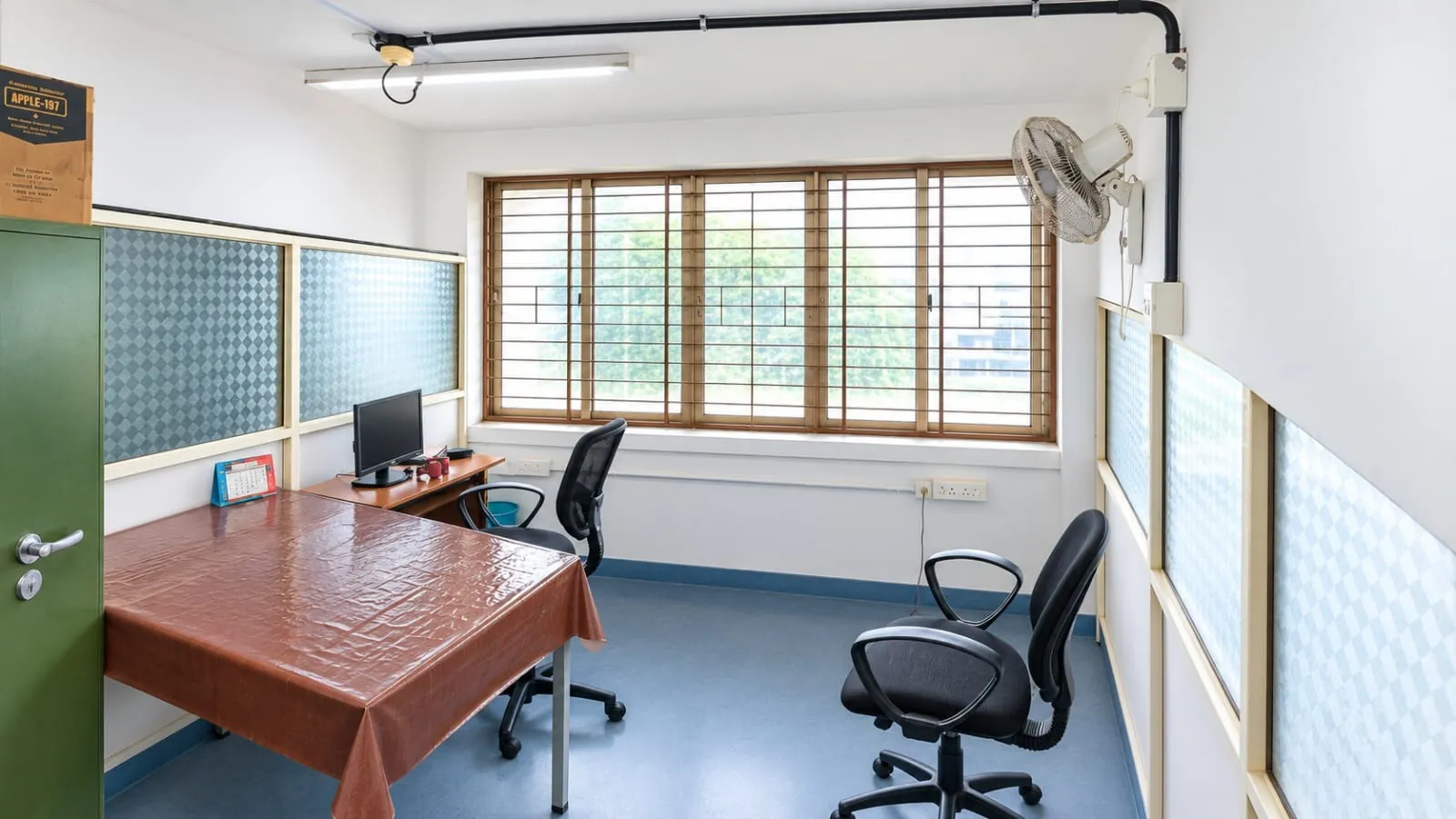 Cabin 1 at TBI MESCE: a desk with a monitor in the corner, a table, two black office chairs and a wide window with trees outside